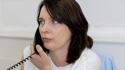 In einem hellen Büro telefoniert eine Frau, ihre Mimik zeigt Nachdenklichkeit und Aufmerksamkeit während des Gesprächs.