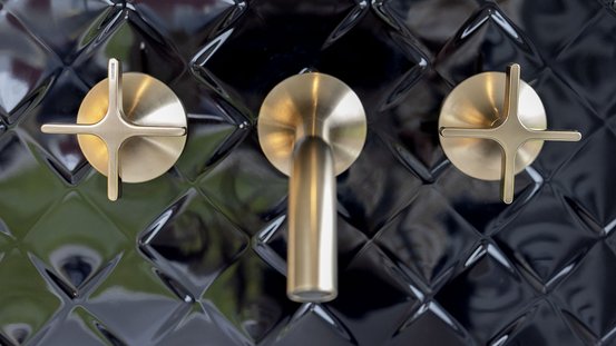 Drei goldene Wasserhähne sind an einer glänzenden, schwarzen Fliesenwand montiert, die ein modernes Design ausstrahlt.