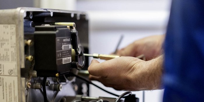 Hände eines Fachmanns, die an einem elektrischen Gerät arbeiten, um Kabel und Anschlüsse zu überprüfen und zu reparieren.