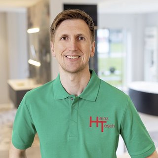 Ein lächelnder Mann in einem grünen Poloshirt steht in einem modernen Raum mit hellen Wänden und eleganten Möbeln.