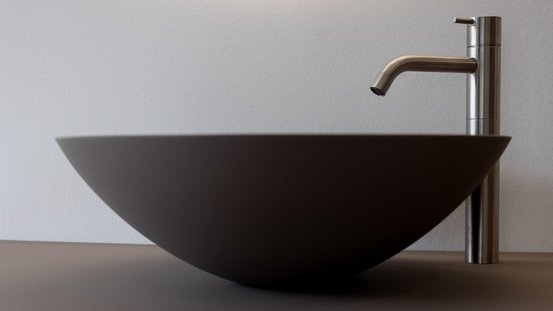 Eine moderne, runde Waschschüssel aus dunklem Material steht auf einer glatten Oberfläche neben einem eleganten Wasserhahn.