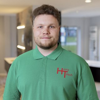 Ein junger Mann mit einem freundlichen Lächeln trägt ein grünes Poloshirt mit dem Namen Heinz Tesch darauf.