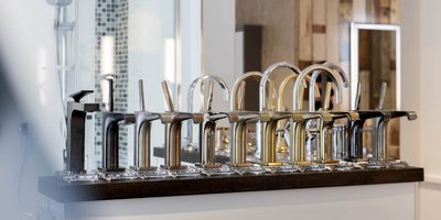 Verschiedene stilvolle Wasserhähne aus Metall stehen nebeneinander, jeder mit einzigartigem Finish und Form, in einem hellen Raum.