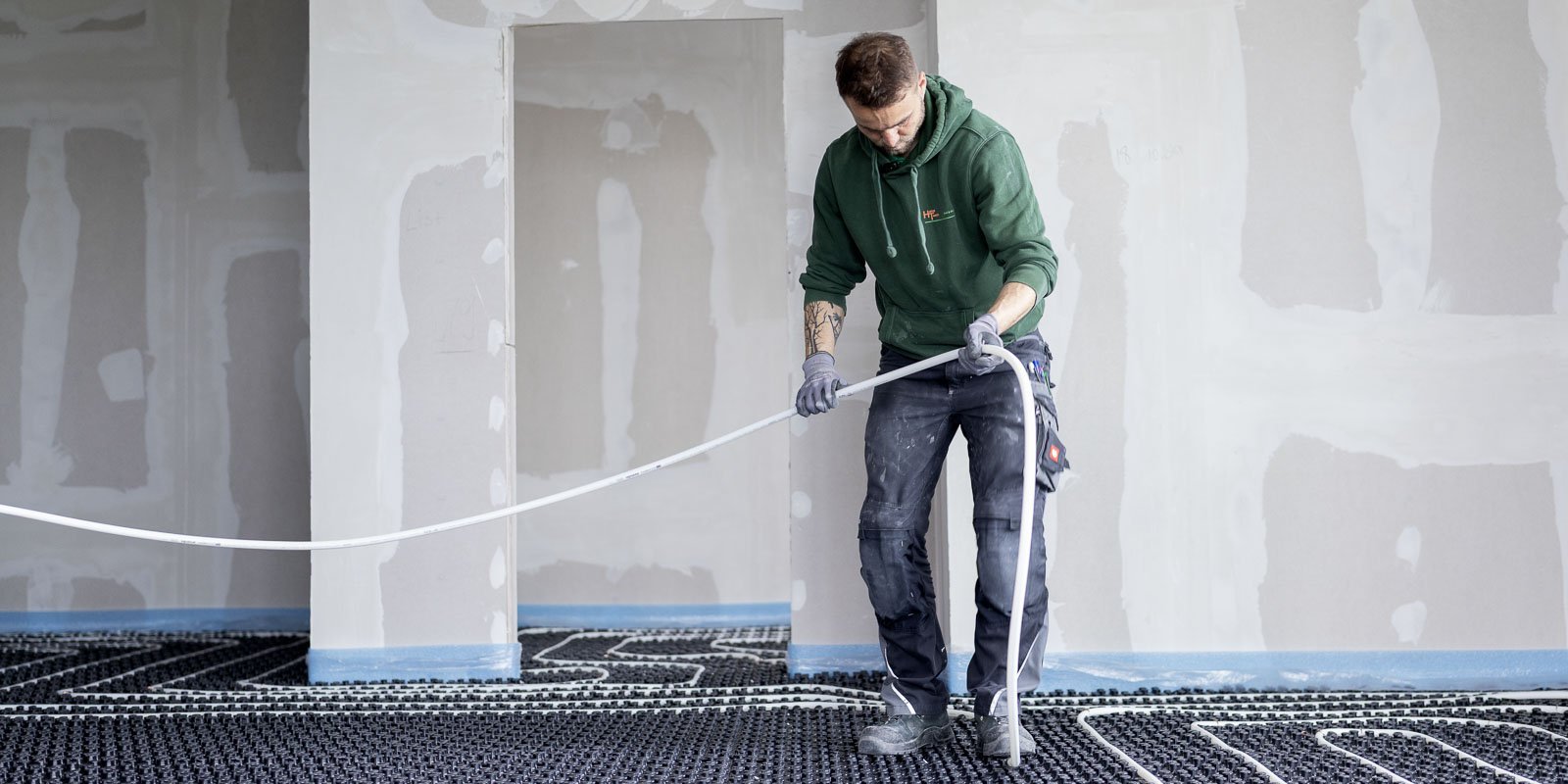 Ein Handwerker verlegt sorgfältig Rohre auf einem neuen Fußboden, um die Heizungsinstallation vorzubereiten.