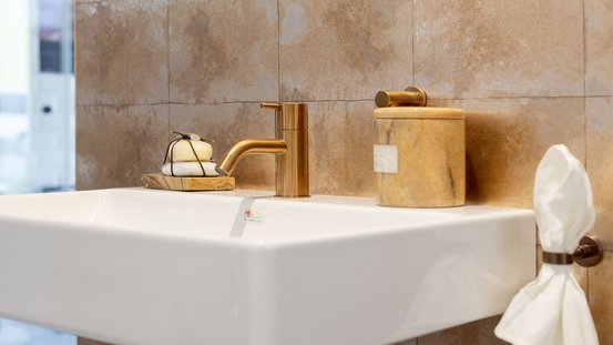 Das moderne Waschbecken zeigt eine stilvolle Kombination aus weißen und goldenen Elementen, ergänzt durch dekorative Seifen.
