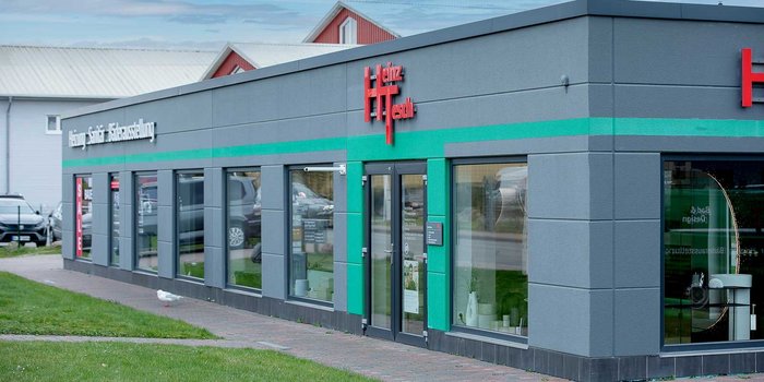 Ein modernes Geschäft mit großen Fenstern, das eine grüne Akzentlinie und den Namen 'Heinz Tesch' in leuchtendem Rot trägt.