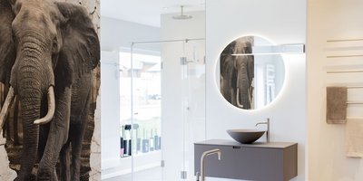 Ein elegantes Badezimmer mit einem großen Spiegel und einem stilvollen Waschbecken, das von einem Elefantenmotiv an der Wand ergänzt wird.