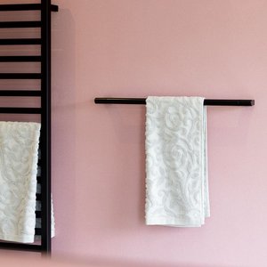 Ein eleganter Handtuchhalter aus schwarzem Metall mit zwei weißen, kunstvoll bestickten Handtüchern an einer zarten rosa Wand.