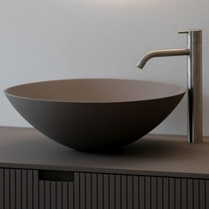 Das stilvolle, runde Waschbecken aus mattem Braun wird von einem schlanken, silbernen Wasserhahn ergänzt, der an einer Wand montiert ist.