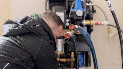 Fachmann überprüft Heizungsrohre und -anschlüsse Der Handwerker überprüft sorgfältig die Rohre und Anschlüsse einer Heizungsanlage in einem modernen Raum.