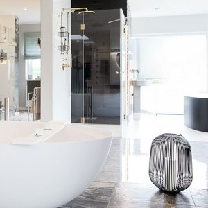 Der Raum zeigt eine helle, minimalistische Einrichtung mit einer weißen Badewanne und einem dekorativen, gestreiften Hocker.