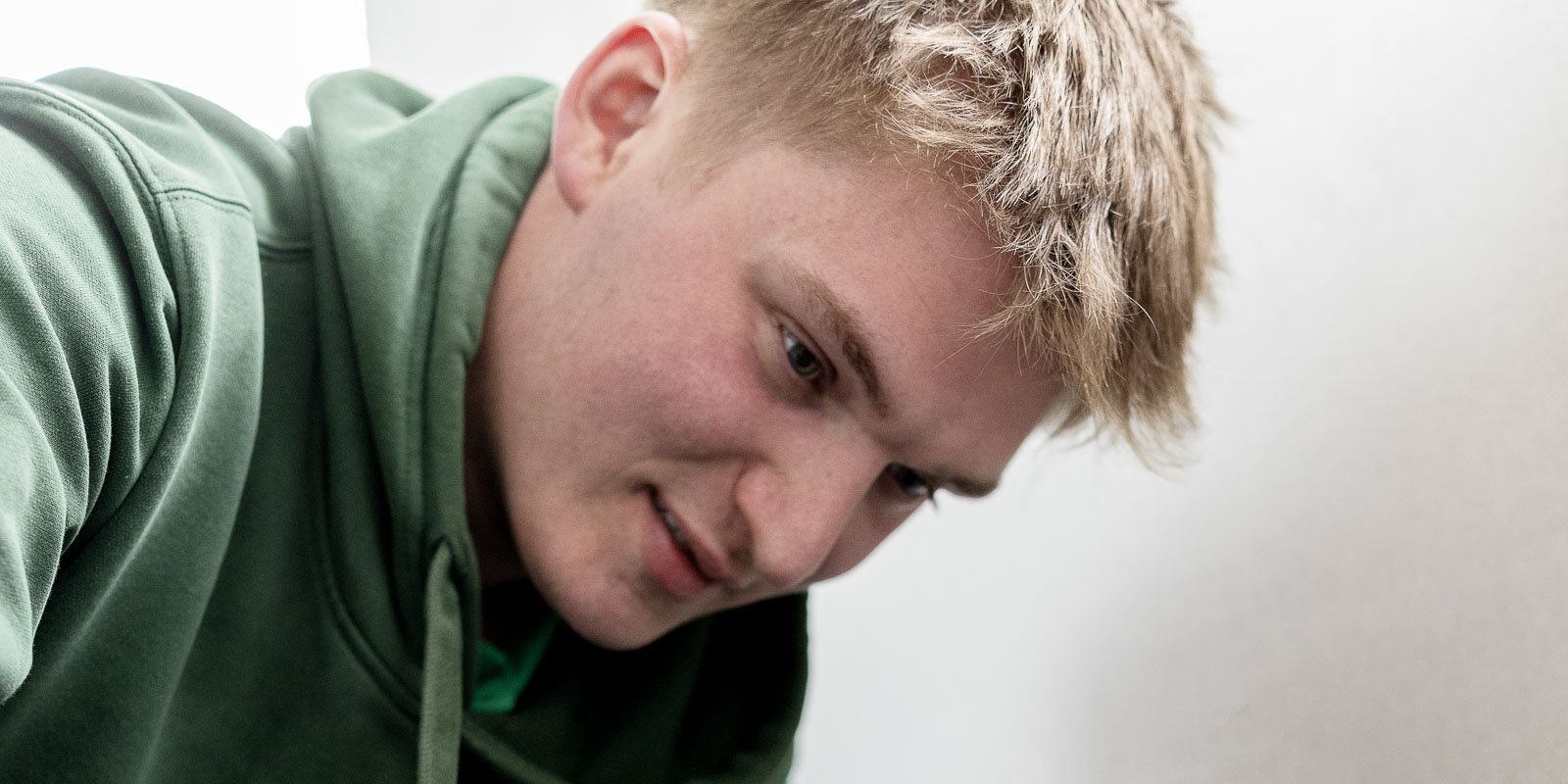 Der Mann mit dem grünen Pullover hat einen nachdenklichen Gesichtsausdruck, während er sich auf eine Aufgabe konzentriert.
