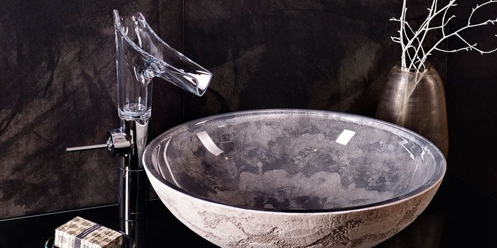 Das Bild zeigt ein kunstvolles Waschbecken mit einem klaren Wasserhahn, ergänzt durch eine schlichte Vase mit weißen Zweigen.