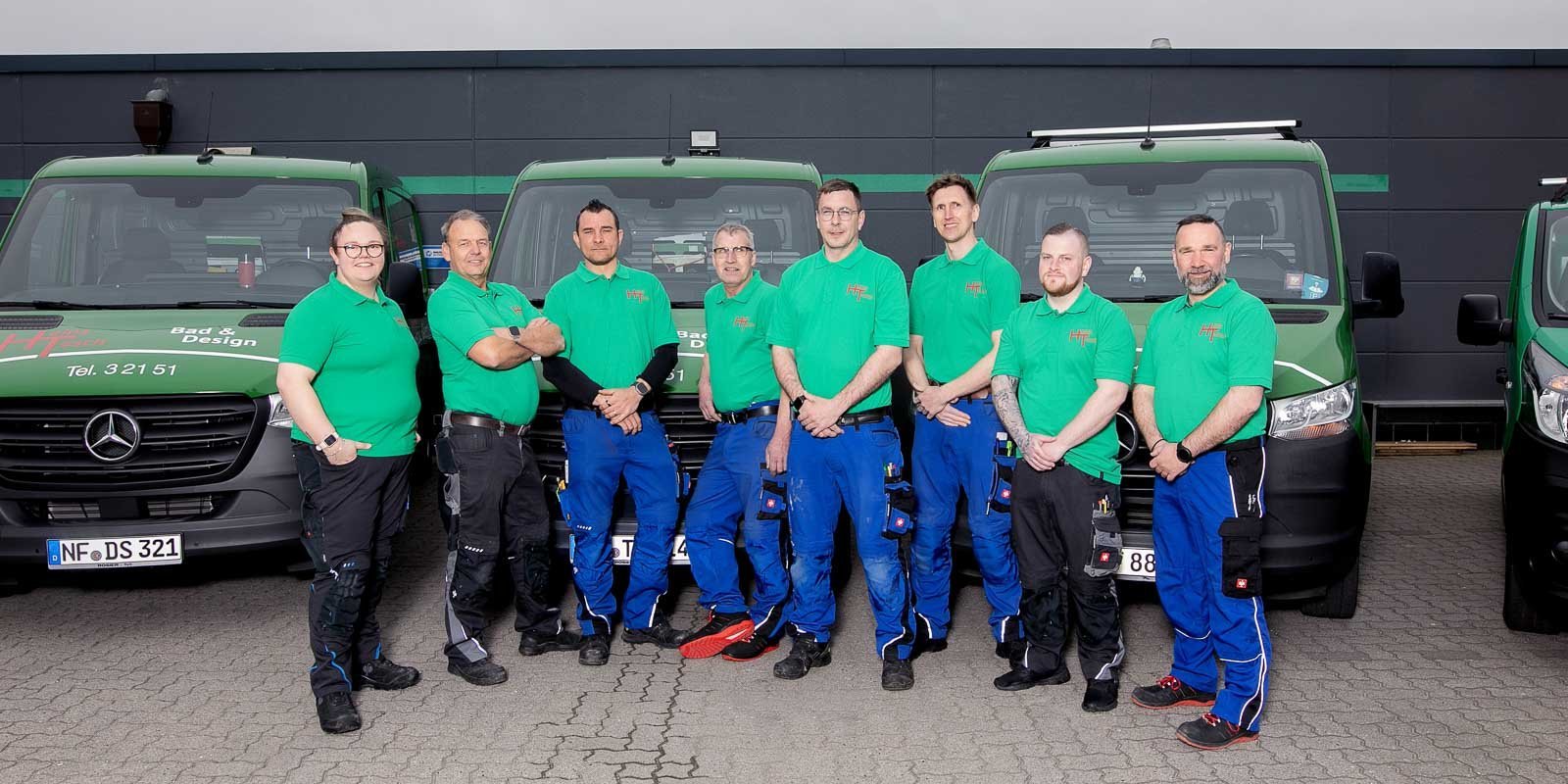 Die Mitarbeiter posieren in Arbeitskleidung vor ihren Fahrzeugen, die mit dem Firmenlogo und Kontaktdaten versehen sind.