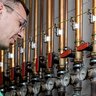 In einem technischen Raum arbeitet ein Mann an einer Installation mit Kupferrohren und verschiedenen Ventilen.