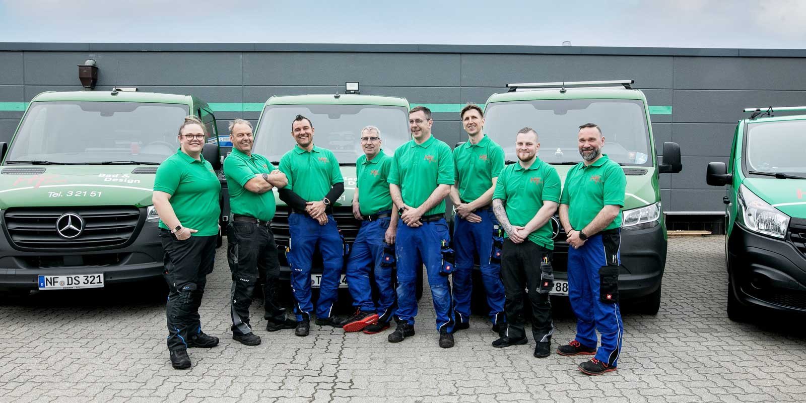 Die Mitarbeiter posieren in Arbeitskleidung vor ihren Fahrzeugen, die mit dem Logo ihrer Firma versehen sind, und strahlen Freundlichkeit aus.
