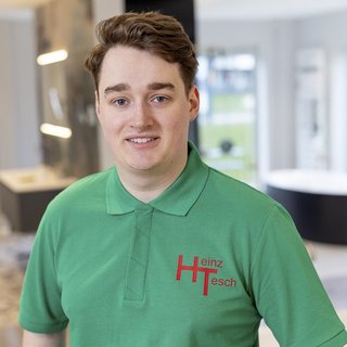 Ein junger Mann mit lockigem Haar trägt ein grünes Poloshirt mit dem Logo 'Heinz Tesch' und lächelt freundlich.