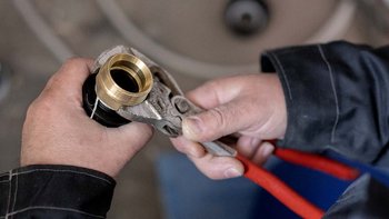 Hände einer Person, die eine Zange benutzen, um einen goldenen Rohranschluss zu fixieren, während sie konzentriert schaut.