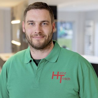 Ein Mann mit einem freundlichen Lächeln trägt ein grünes Poloshirt mit dem Logo 'Heinz Tesch' darauf.