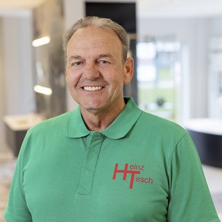 Der Mann mit kurzen Haaren und einem freundlichen Lächeln trägt ein grünes Shirt mit dem Namen 'Heinz Tesch' auf der Brust.
