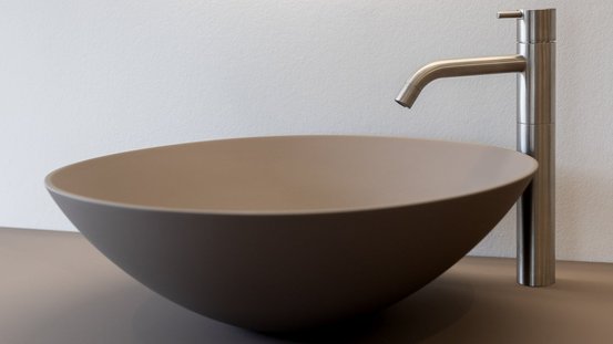 Eine moderne, runde Waschschüssel aus mattem Material steht neben einem eleganten, silbernen Wasserhahn.