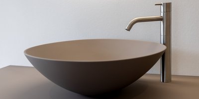 Eine moderne, runde Waschschüssel aus mattem Material steht neben einem eleganten, silbernen Wasserhahn.